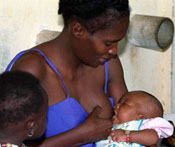 Woman breastfeeding a young baby, a young child seated next to the mother looks on