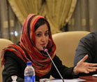 Iranian woman wearing head scarf seated at conference table, woman speaks into microphone