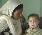 Pakistani woman seated watches a boy toddler on her lap