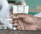 Hand holding burnt down cigarette rests on table, glass in background