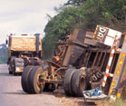 Large truck rolled over on side on the side of a paved road, wheels and axels detached, truck severely damaged