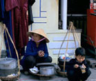 Vietnamese woman and child crouche next to pots on the sidewalk