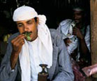 Man with droopy eyes stuffs handful of khat into his mouth
