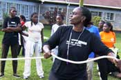 African woman in foreground in athletic wear holds rope, whistle around her neck, more women in background also wearing athletic