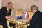 Dr Roger I Glass signs agreement on table, Russian representative across table signs, US and Russian flags on table