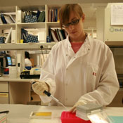 Tessa Lecuyer in white lab coat and gloves observes samples in lab
