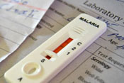 Close up of white malaria test showing red indicator sitting on top of sheet of paper with title laboratory