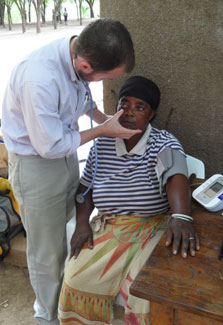Dr. John Stanifer examines seated female patient outdoors
