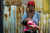 Woman stands while nursing a baby, solemn frown on her face