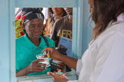 Medical worker in white coat distributes medications through a service window to an older woman