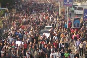 Crowded street in Egypt packed with protesters walking, some abandoned cars in road, some carry signs