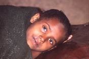 Young Ethiopian child rests on its side, wrapped in a blanket, looks into camera