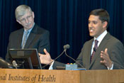 Dr. Rajiv Shah speaks into microphone at podium, Dr. Francis Collins stands next to him