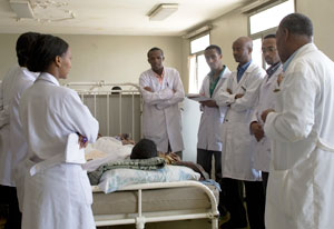Medical students in white lab coats gather and discuss around patient bed in hospital