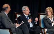 NIAID Dir Fauci speaks on stage, Fogarty Dir Glass and NHLBI Dir Shurin look on