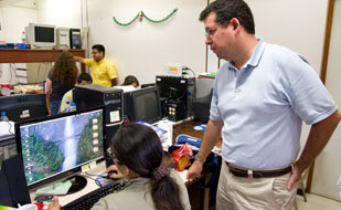 David Snyder for Fogarty/NIH, Woman seated works on computer, man stands behind her looking on, in busy lab