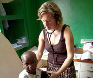Dr Manning in an exam room with stethoscope in ears holds it to a young boy’s back, she looks down at him