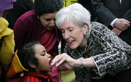 Kathleen Sebelius administers polio vaccine to young child, woman looks on closely from behind