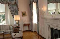 Living room with view of fireplace and tall windows hung with curtains