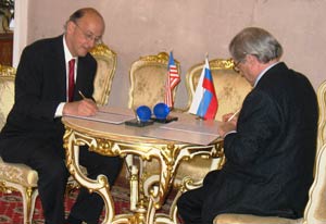 Dr Roger I Glass signs agreement on table, Russian representative across table signs, US and Russian flags on table