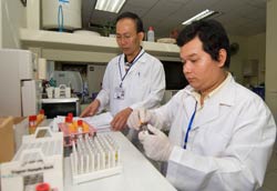 Two male researchers in white coats in lab wearing medical golves work with samples in test tubes