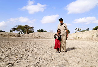 woman and her child stand at the bottom of a basin that used to be the community watering hole near the small town of Aje, Ethiopia