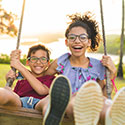 Photo by Pallyana Ventura/Getty Images. Two smiling children on swing outdoors.