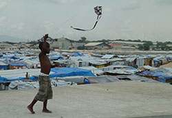 Boy flies a kite, refugee camp in background, after 2010 earthquake in Haiti