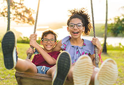 Two smiling children on swing outdoors.