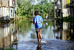 Woman walks through flooded street, water up to her ankles, 2-story wooden buildings on either side of street