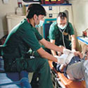 Two medical workers in an organized ambulance work with an injured patient reclined on a mobile stretcher.