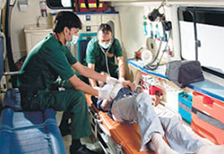 Two medical workers in an organized ambulance work with an injured patient reclined on a mobile stretcher