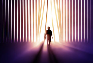 Silhouette of person walking through vertical blinds toward a bright light.