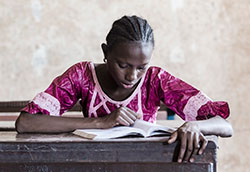 A young woman seated at a desk reads a book in a classroom.