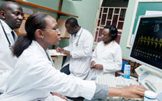 Medical workers in white coats, one adjusts computer with large monitor