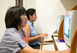 Two women seated at computer work stations view information on monitors