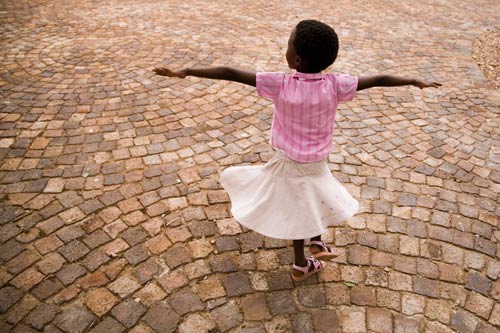 young girl in skirt twirls on brick-paved street, arms fully extended