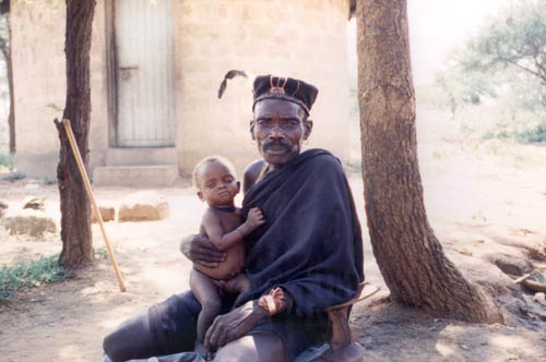 Man seated on dusty ground, infant in his lap