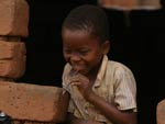 Smiling young Malawian boy leans out of bare window of rough brick building