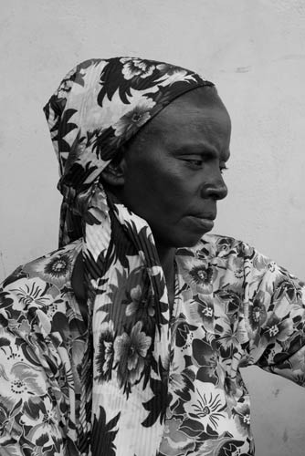 black and white photo of profile of older Tanzanian woman wearing flowered head scarf and top