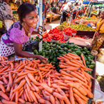 woman smiling surrounded by vegetables at a market