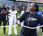African woman in foreground in athletic wear holds rope, whistle around her neck, more women in background also wearing athletic