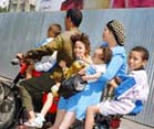 family of father, mother, and four children ride on a small scooter