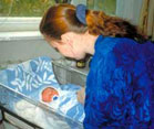 woman nurse bends over a newborn in a plastic hospital crib