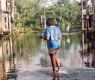 Woman walks through flooded street, water up to her ankles, 2-story wooden buildings on either side of street