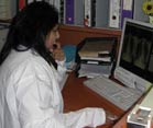 Dr Naidoo in a white lab coat seated at a desk reviews side by side chest x-rays on a computer screen