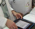 iPad, held by hands or person wearing white lab coat, placed on desk next to paper file