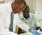 Two men working side by side in a laboratory at a MEPI-supported institution examine samples, one wears white lab coat and glove
