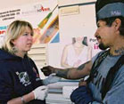 woman wearing plastic gloves holds the arm of a man in front of a mobile health clinic