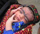 Pakistani baby sleeping wrapped in blanket with grey surma eye makeup along eyebrows and forehead